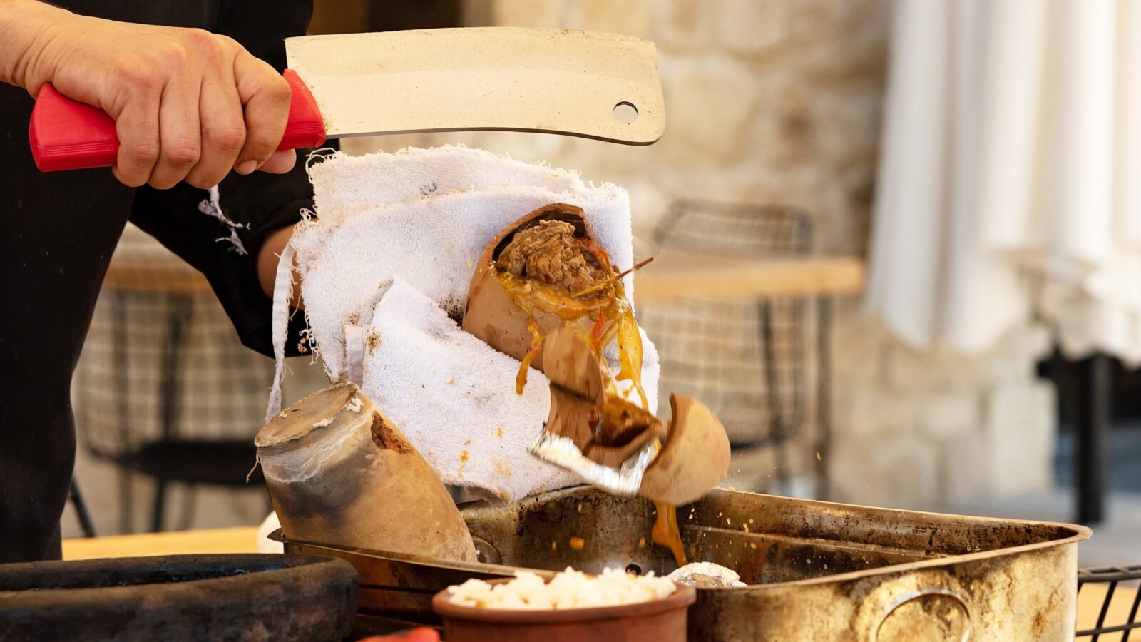 A person slicing open a cooked dish wrapped in cloth with a large knife.
