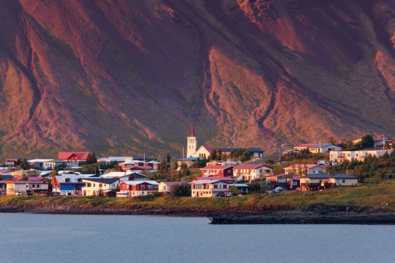 A quaint seaside village with colorful houses nestled at the base of a mountain at sunset.