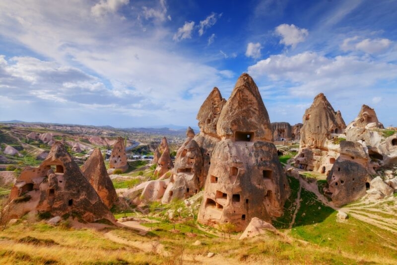 Unique rock formations and ancient cave dwellings under a blue sky in Cappadocia, Turkey, showcasing stunning geological and historical features.
