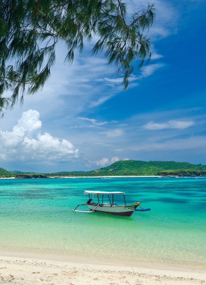 A traditional boat floats on crystal-clear turquoise waters, surrounded by lush green hills and a blue sky dotted with clouds.
