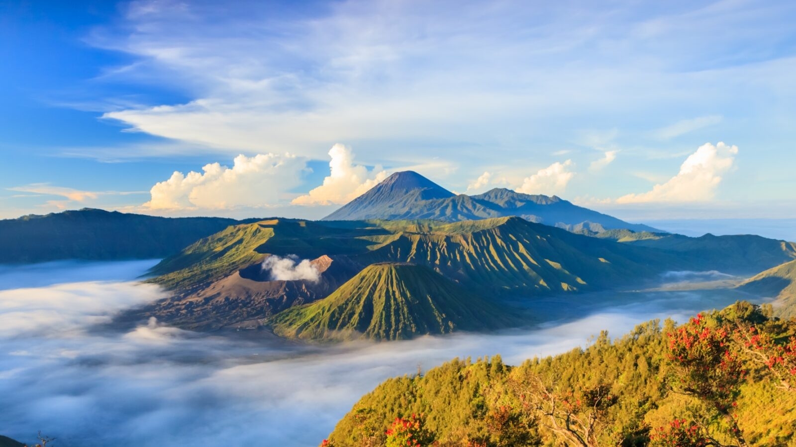 Stunning sunrise over Bromo Tengger Semeru National Park, revealing volcanoes amid dramatic clouds and vibrant green hills.