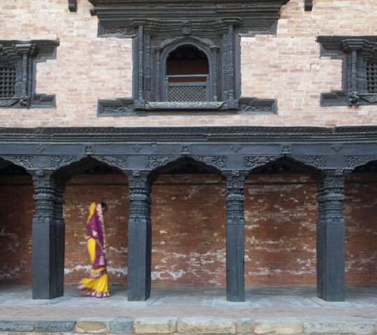 Woman dressed in traditional clothing walking in a corridor of a traditional building in Nepal.