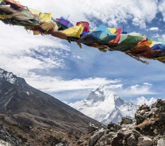 Snowy mountain in the Himalayas with colourful prayer flags in the foreground.