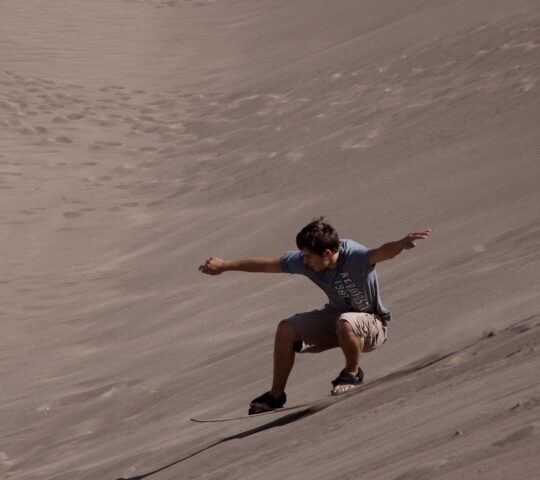 A man sandboarding down a sand dune