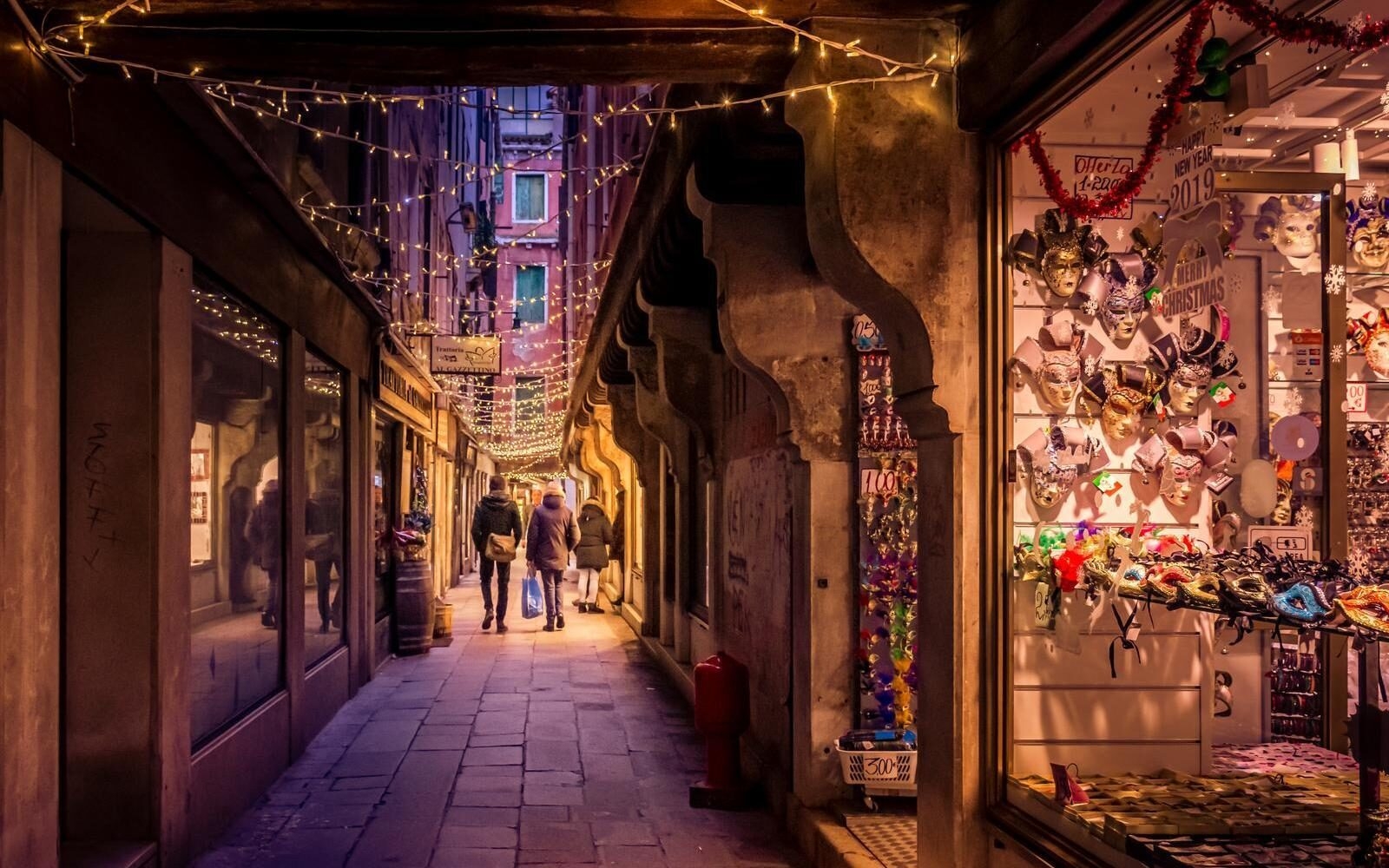 A narrow street in Venice with Christmas lights and shop displays of traditional Venetian masks.