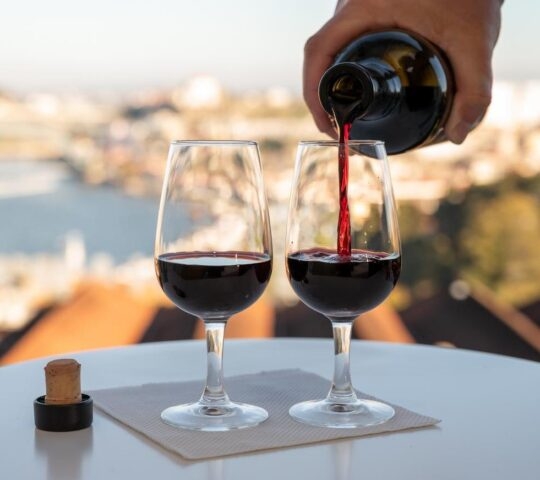 A person pouring wine in a glass with the Douro River in the background.