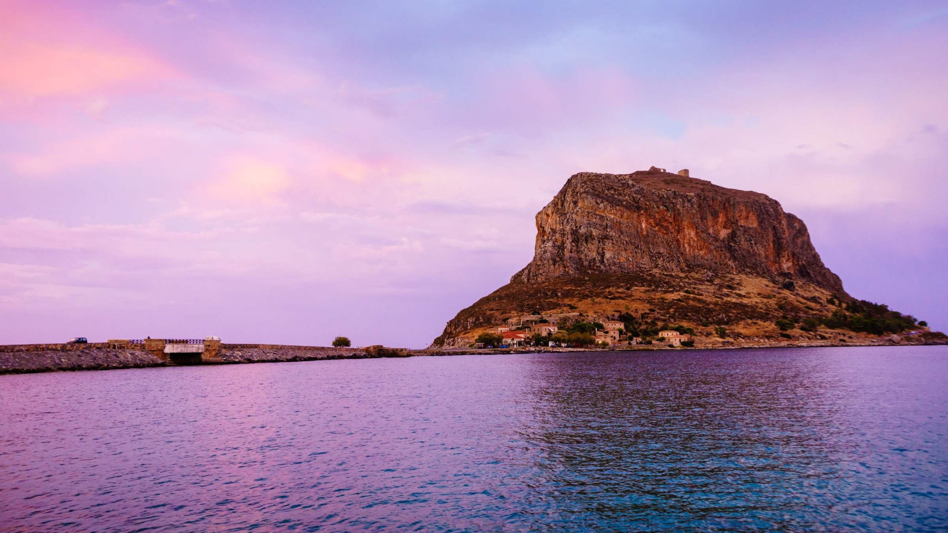 The island of Monemvasia seen at sunset with purple sky reflecting on the ocean