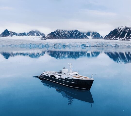 An aerial of Aqua Lares cruising across the water with snowy mountains in the background.