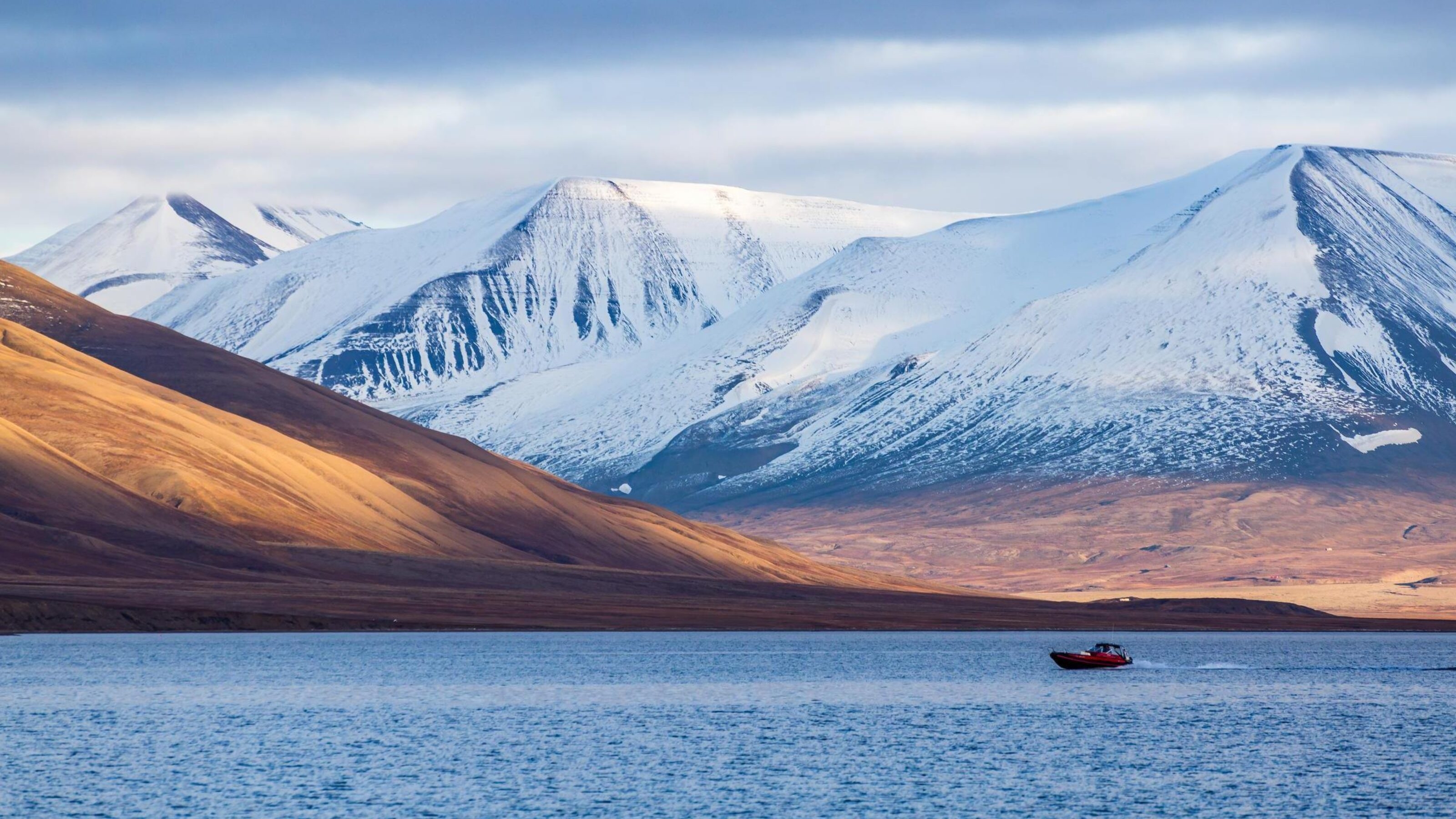 A small boat cruising across the sea in front of snowy mountains.
