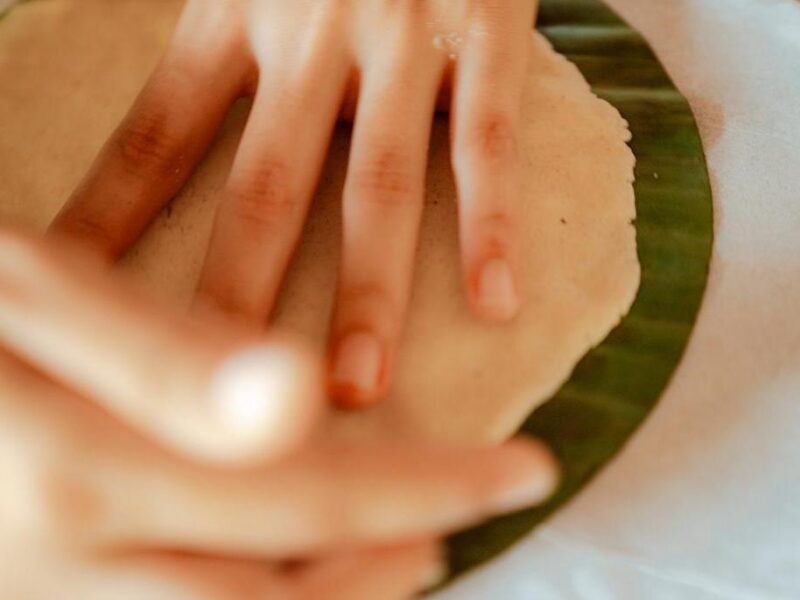 A close-up of hands flattening dough onto a circular green leaf during luxury Family vacations.