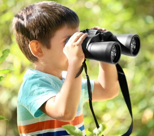 A boy looking through binoculars in the outdoors.