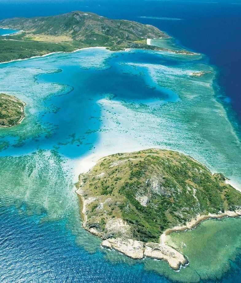 A high-angle aerial view of Lizard Island surrounded by turquoise reefs and deep blue ocean, and an jabiru wading through the wetlands of Kakadu National Park.