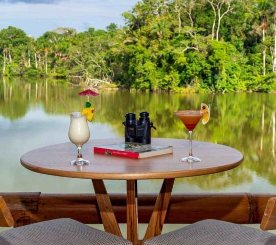 Two cocktails and a pair of binoculars on a table lagoon-side at La Selva Lodge.