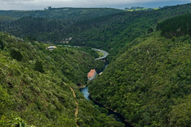 A river flows through a steep valley covered in thick green forest with a white building nestled on the bank.