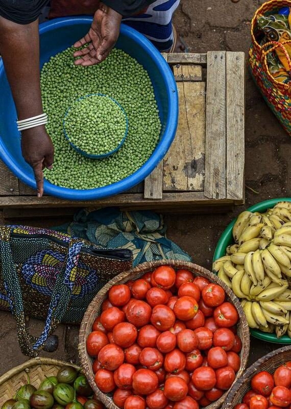 Top-down view of a market vendor's hands near bowls of peas, tomatoes, and bananas in Kigali, Rwanda.