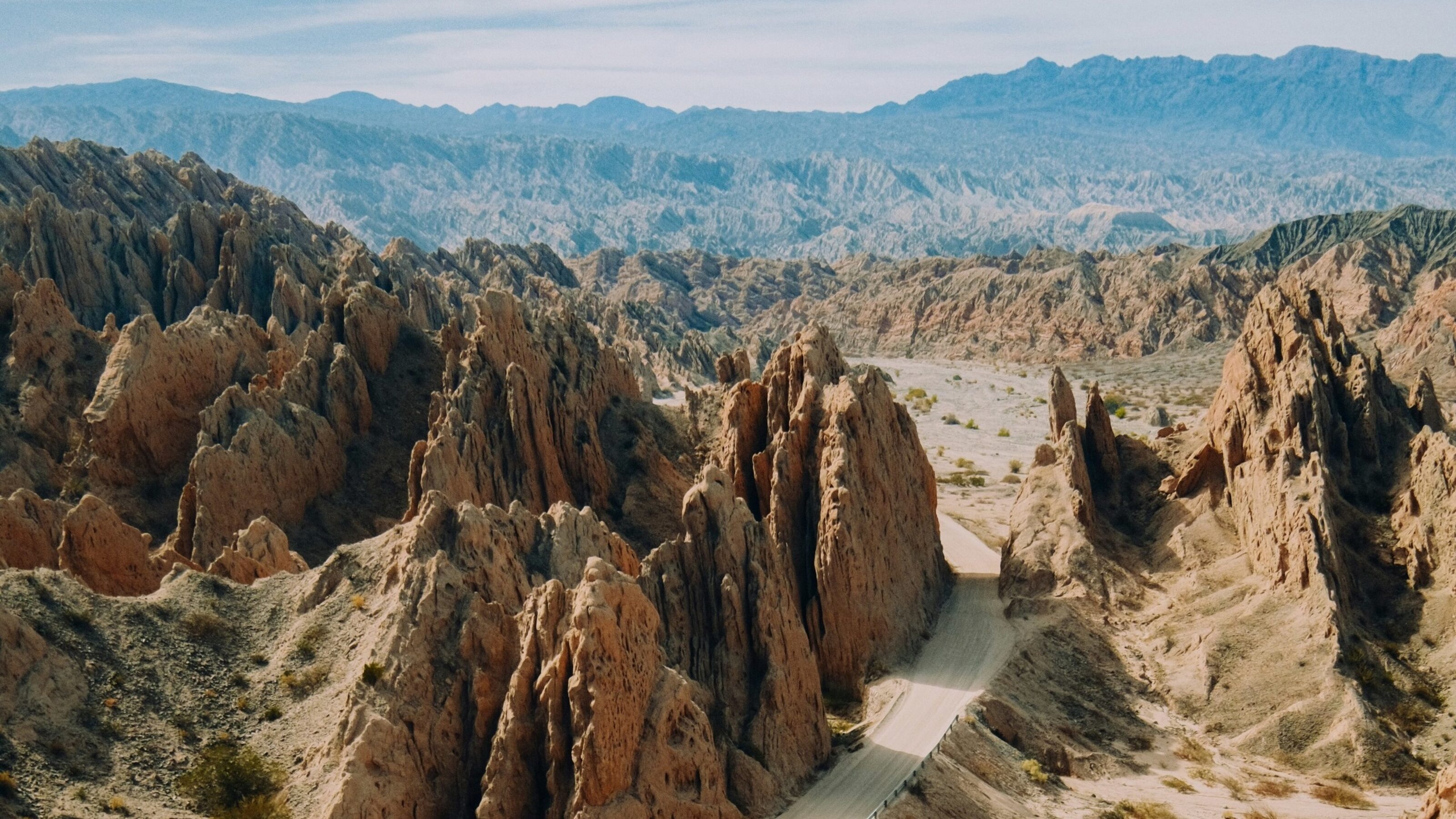 Aerial view of sharp, tan rock formations and a desert road winding through a rugged canyon in Salta, Argentina.