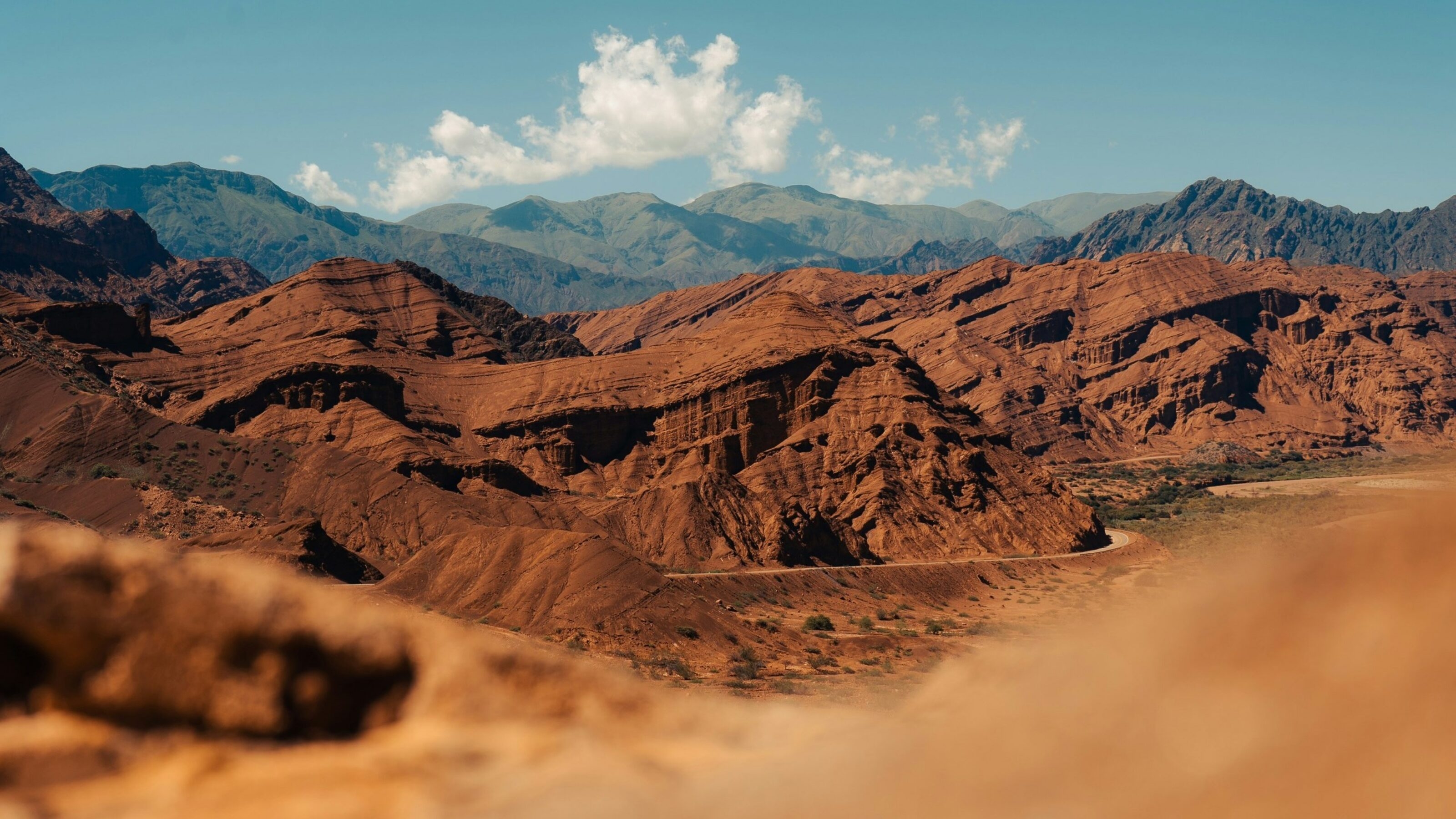 Jagged red rock mountains and desert terrain under a clear sky with distant blue mountain ranges in Salta, Argentina.