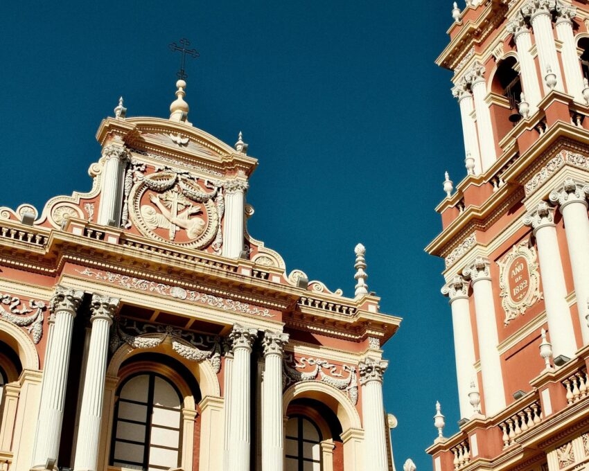 Ornate pink and white colonial church with a tall bell tower and classical columns under a clear blue sky in Salta.