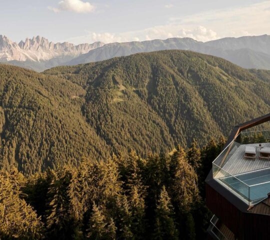 Aerial view of penthouse suite with rooftop pool surrounded by mountains and forest at Forestis Dolomites