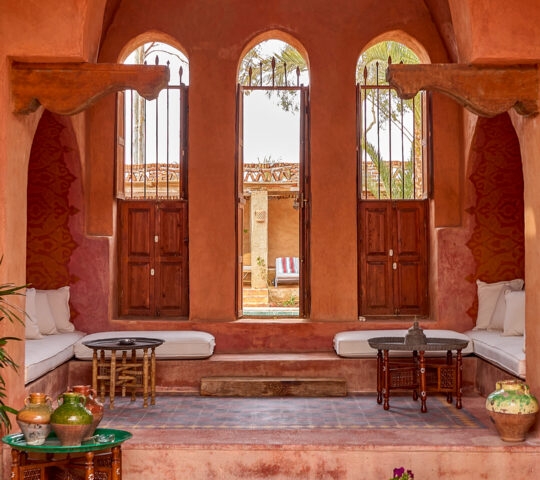 A terracotta-walled courtyard with three arched windows, low cushioned seating, and decorative pottery at Al Moudira Luxor.