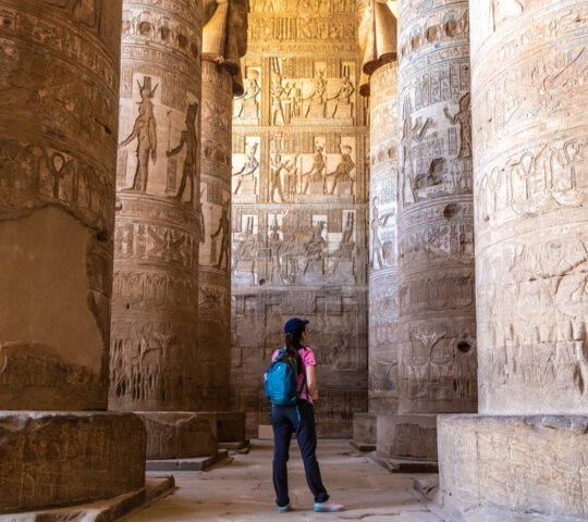Traveler looking at towering ancient Egyptian columns with detailed hieroglyphic carvings in Dendera Temple.