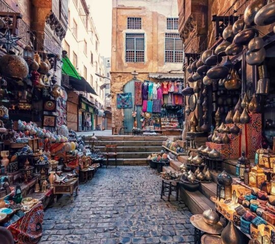 A colorful market street in Cairo lined with intricate hanging lanterns and various traditional metal crafts.