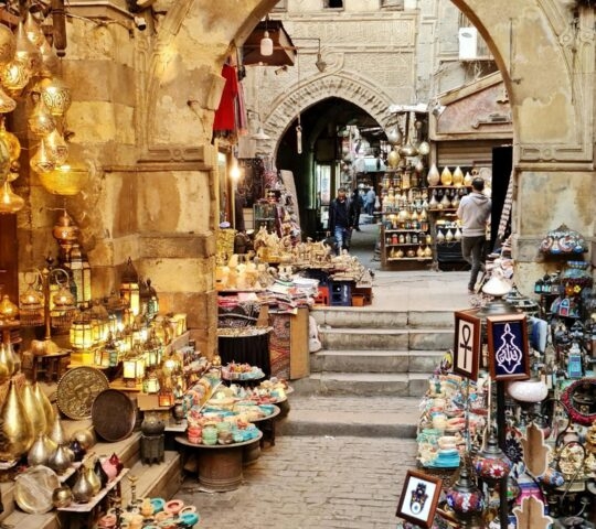 A narrow alleyway in Khan El-Khalili market lined with glowing brass lanterns and colorful Egyptian souvenirs.