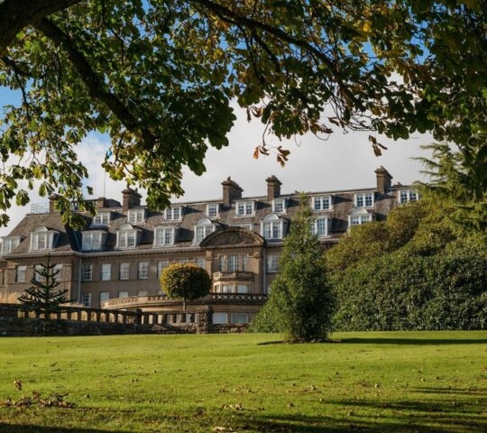 The exterior of Gleneagles hotel in Scotland, half covered by greenery and with a large tree in the foreground