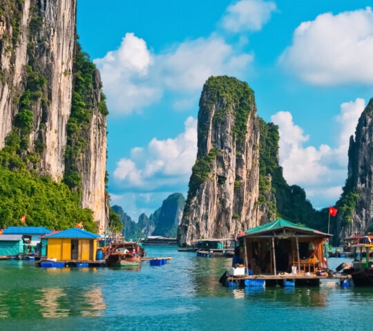 Vibrant floating houses and boats on the water surrounded by massive limestone cliffs in Halong Bay, Vietnam.