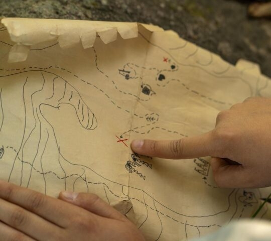 Close-up of hands pointing to a location marked with a red cross on a crinkled paper map.