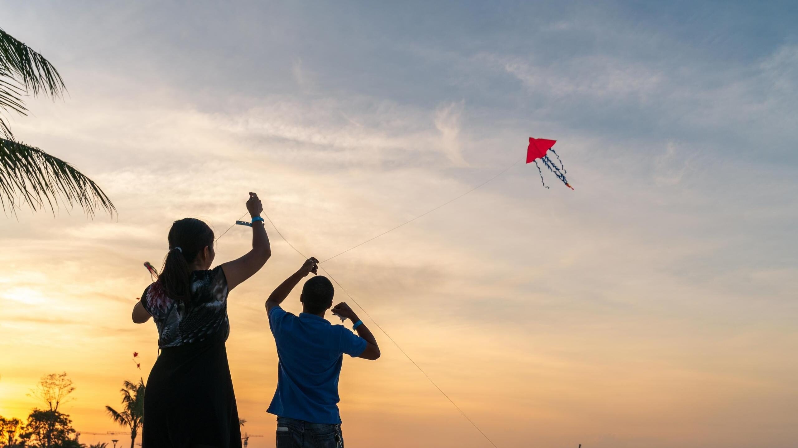 Silhouette of two people flying a red kite on a beach during a vibrant yellow and orange sunset.