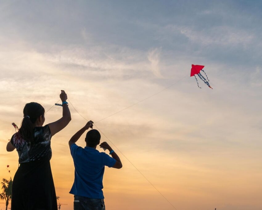 Silhouette of two people flying a red kite on a beach during a vibrant yellow and orange sunset.