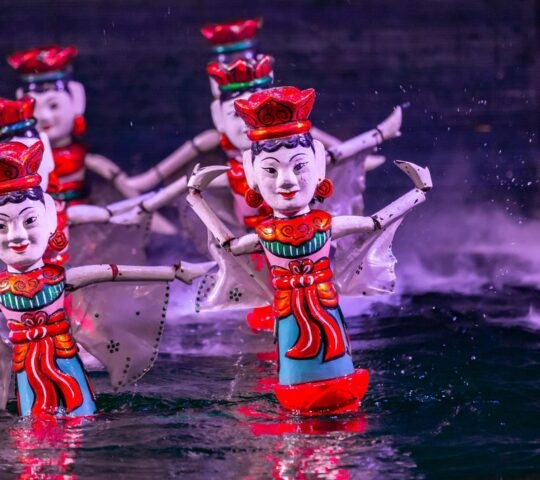 Colorful traditional Vietnamese water puppets performing on a stage of water with mist in the background.