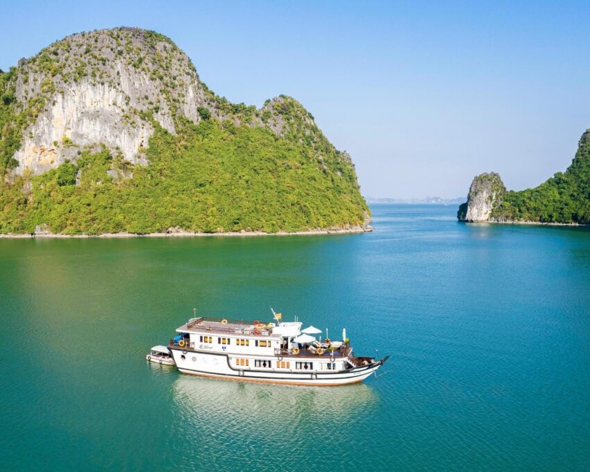 Bhaya Legend cruise ship sailing through turquoise waters and limestone islands in Ha Long Bay, Vietnam.