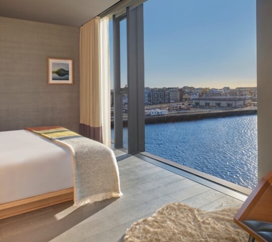 Modern bedroom at The Reykjavik Edition with a large window showing a waterfront view of Reykjavik, Iceland.