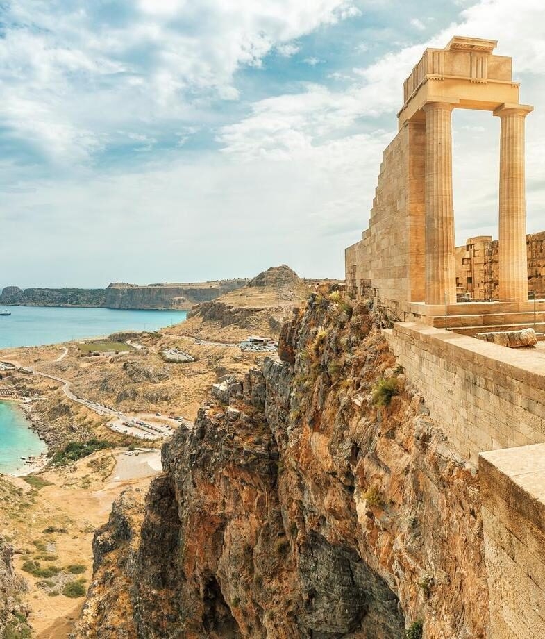 Ancient ruins on a cliffside overlooking the coast of Rhodes, and a view from a wooden boat deck towards the white Cycladic architecture of Piso Livadi harbour in Paros.