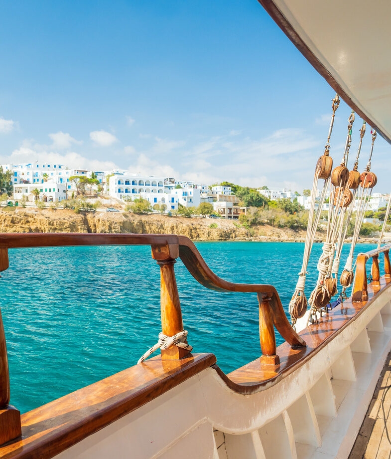 Ancient ruins on a cliffside overlooking the coast of Rhodes, and a view from a wooden boat deck towards the white Cycladic architecture of Piso Livadi harbour in Paros.