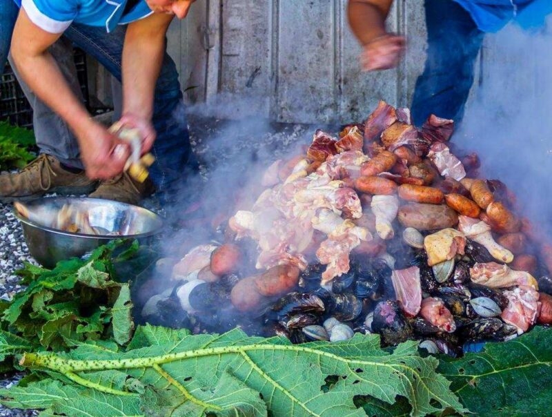 A steaming pile of shellfish, chicken, and potatoes being prepared outdoors on leaves.