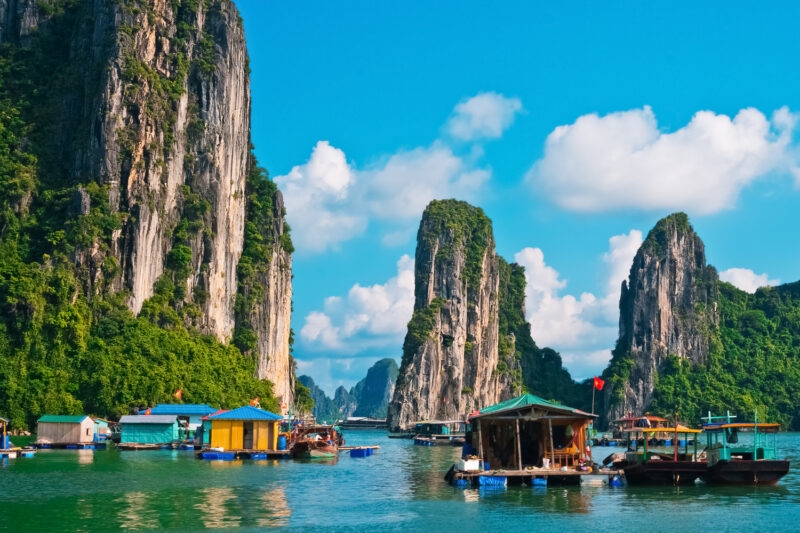 Brightly colored floating houses and boats in Halong Bay, Vietnam, with massive limestone cliffs in the background.