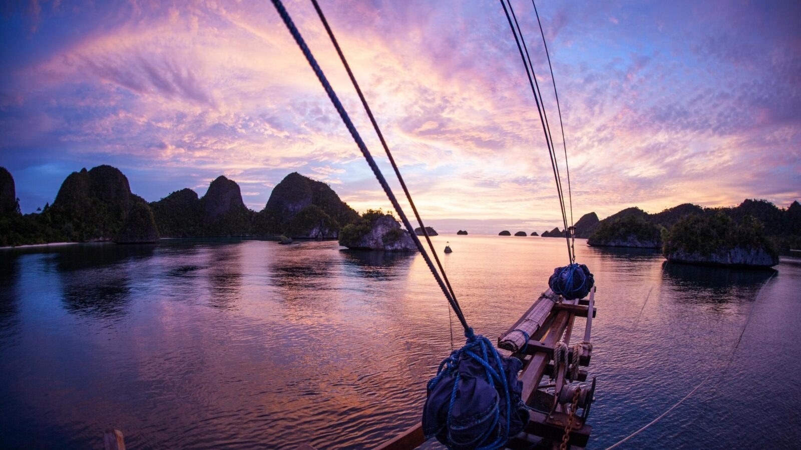 View from the front of a wooden boat looking out at a purple sunset over tropical islands.