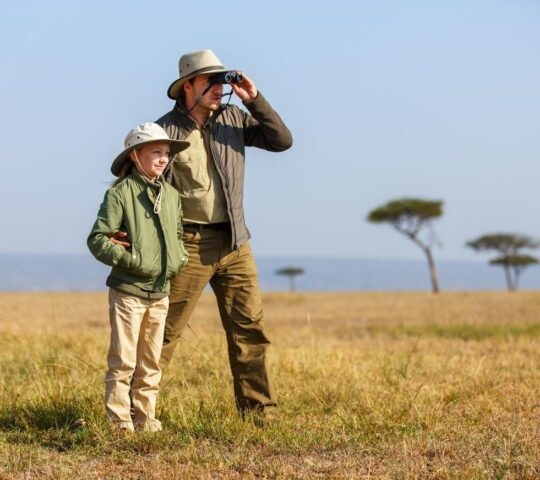A father and daughter looking for wildlife through binoculars in the African savannah