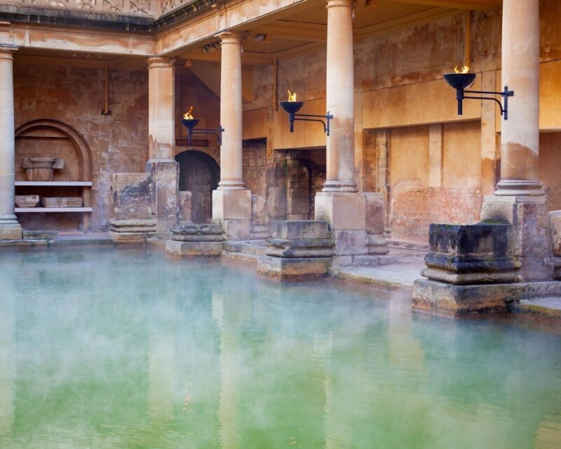 Wide view of the open-air Great Bath in Bath, England, featuring columns and a surrounding balcony.