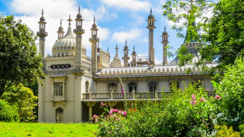 The ornate white domes and minarets of the Royal Pavilion in Brighton viewed from a green garden.