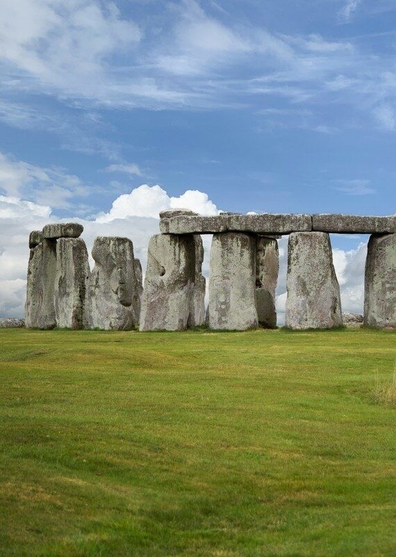 Massive standing stones of Stonehenge arranged in a circle on a green field under a blue sky.