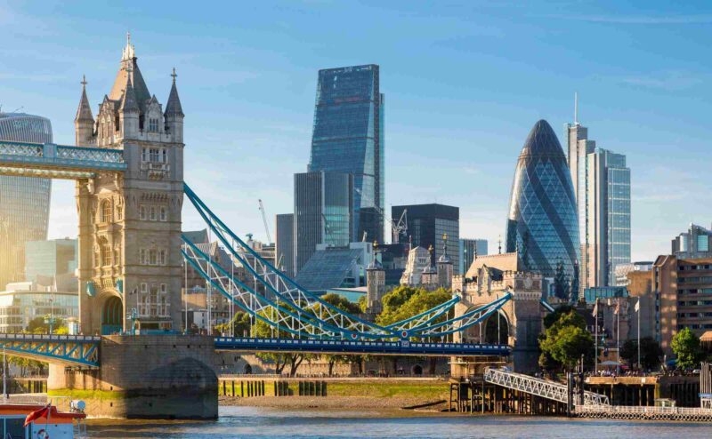 Tower Bridge with its blue suspension cables in the foreground and modern London skyscrapers behind it.