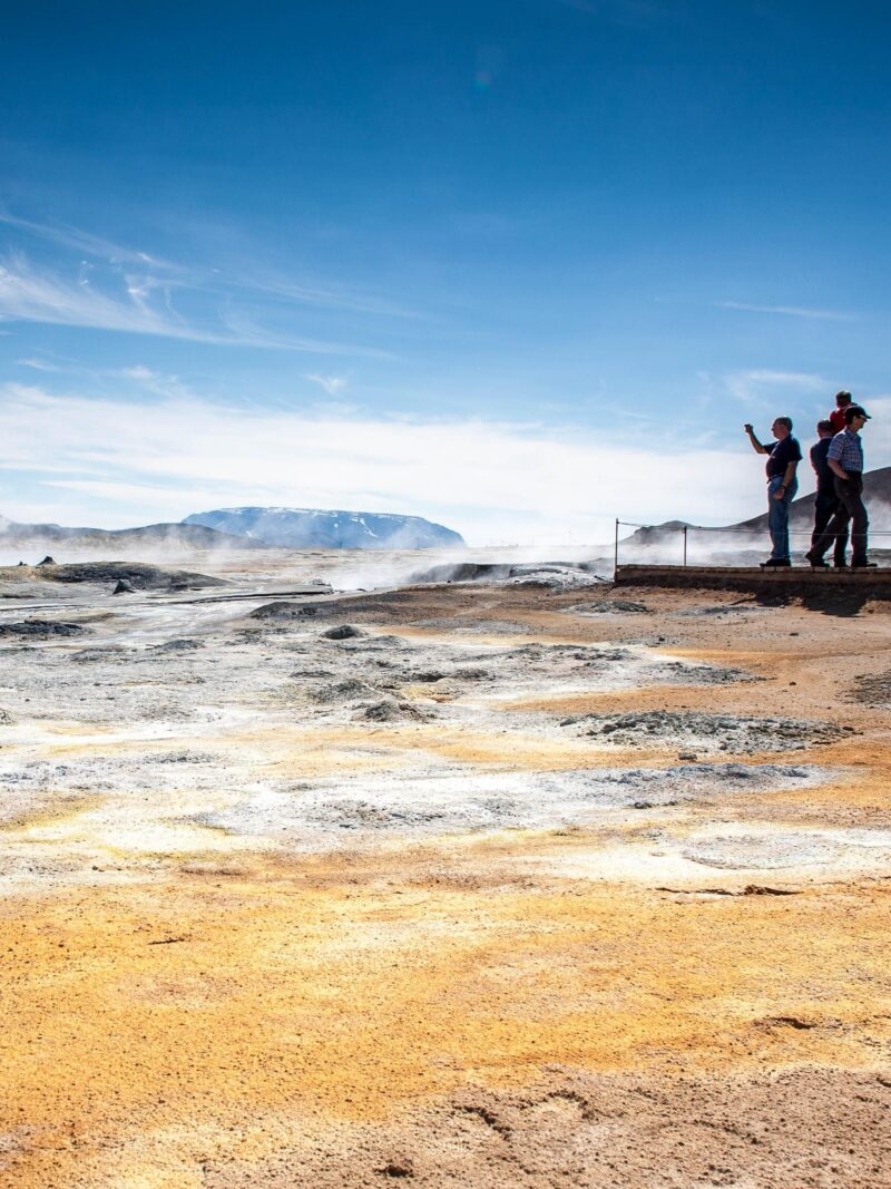 People observing steam rising from geothermal mud pots in a volcanic landscape on an Iceland family vacation.