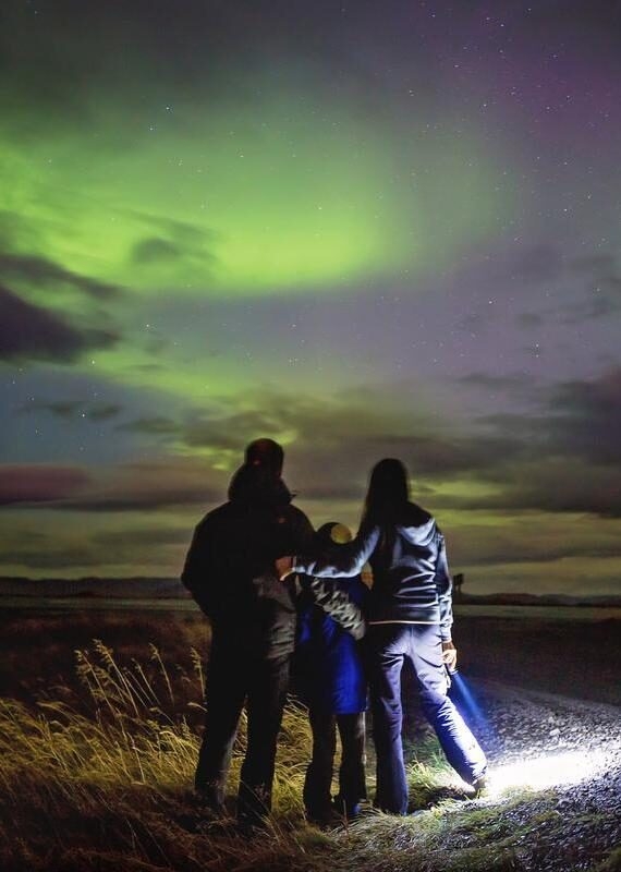 Family silhouette looking at the green northern lights in a night sky during an Iceland family vacation.
