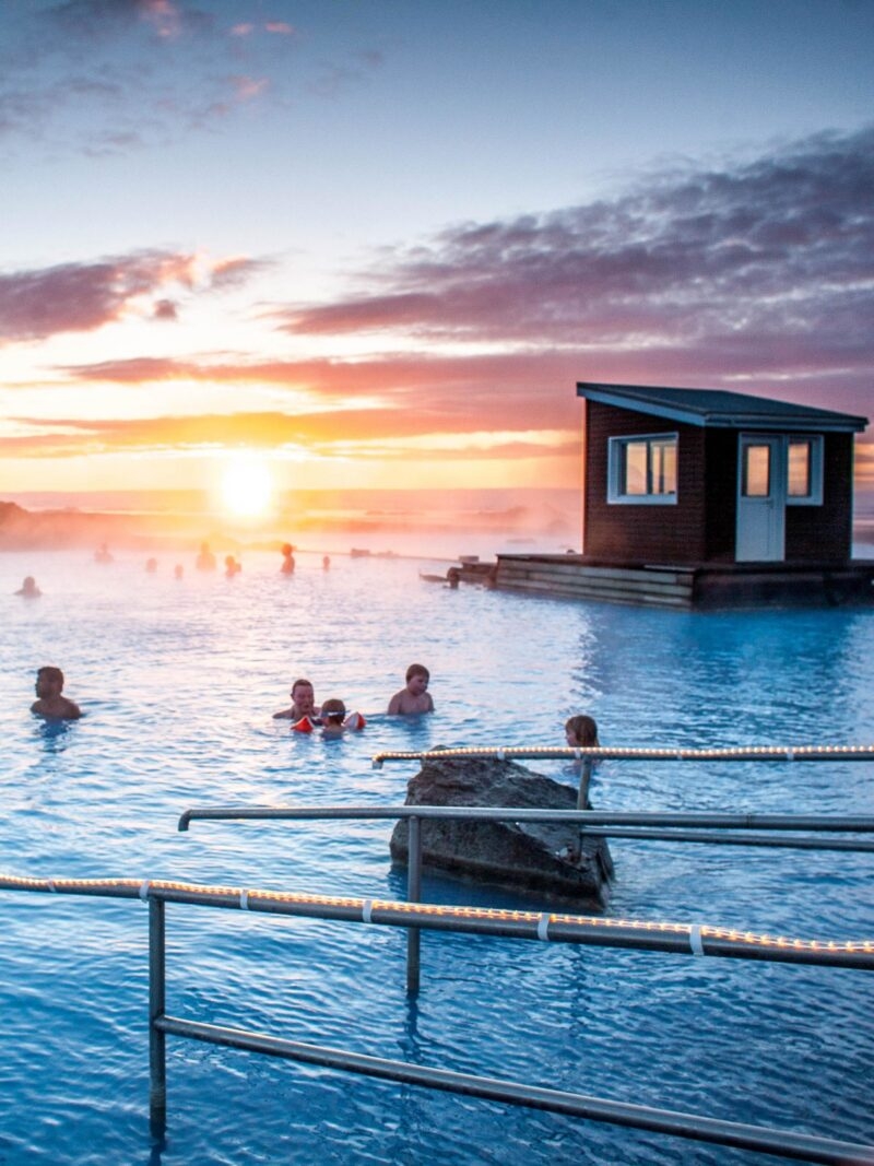 People swimming in a geothermal spa at sunset during an Iceland family vacation.