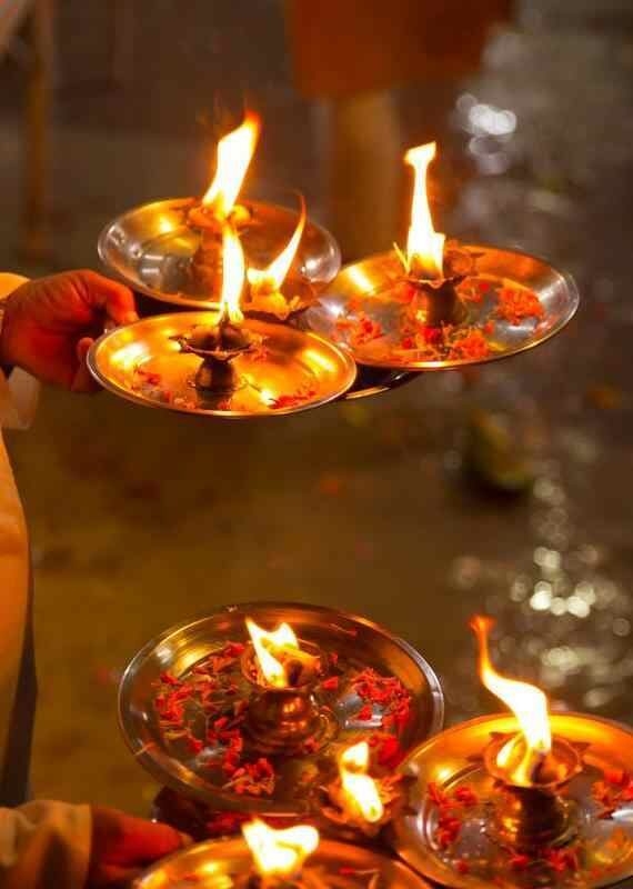 Multiple burning oil lamps on metal trays decorated with red flower petals held during a religious Aarti ceremony.