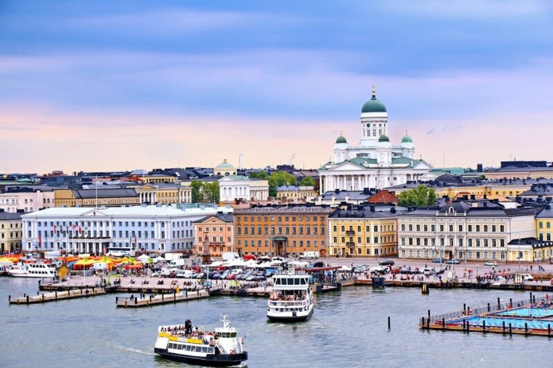 Aerial view of Helsinki harbor showing the white cathedral, colorful waterfront buildings, and boats on the blue water.
